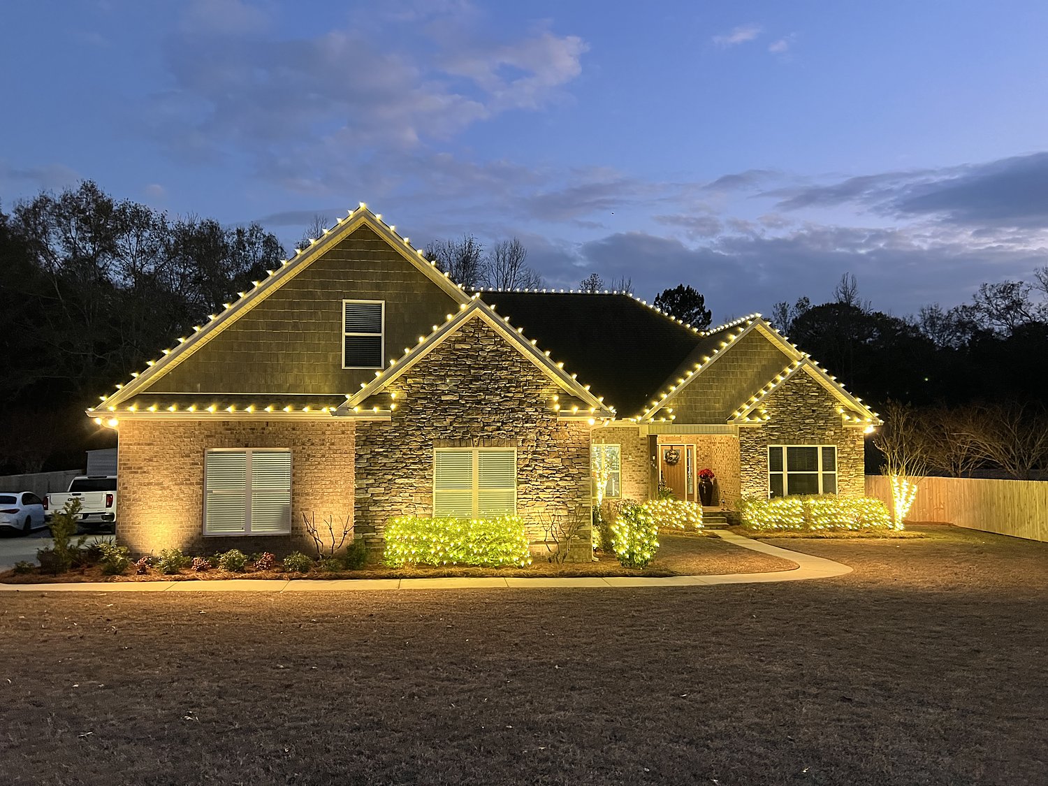 Home with full warm white roofline and lit landscaping at dusk