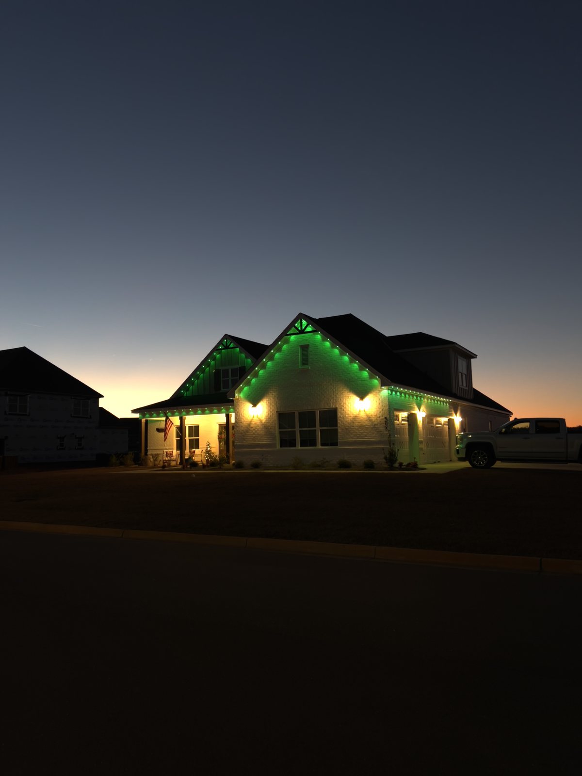 Brick home lit green with permanent lighting at dusk